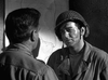 A helmeted soldier in a military jacket speaks gravely to another man before a wall map in this dramatic black-and-white scene from the World War II action film "Suicide Battalion (1958) DVD.