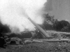 Experience the excitement of classic WWII cinema with Suicide Battalion (1958) on DVD, featuring intense artillery fire amidst rocky terrain, scattered stones, and a dramatic backdrop of trees.