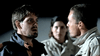 Two men stand face-to-face in a tense confrontation as a concerned woman watches nearby. All three are outdoors at night in jackets—capturing the suspense of "The Bone Snatcher (2003) DVD.
