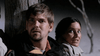 A man and woman lean against a wooden post at night, looking anxious. The dark, blurry background adds suspense to "The Bone Snatcher (2003) DVD," a rare, hard-to-find early 2000s horror film.