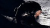 A person covered in black oil crawls on muddy ground at night, their face barely lit—a chilling image evoking early 2000s horror, like "The Bone Snatcher (2003) DVD," a rare and hard-to-find movie for genre collectors.