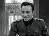 A man in military uniform smiles and talks while seated indoors in this black-and-white WWII drama. "Under Fire (1957) DVD" offers a rare, hard-to-find movie with a window showing trees in the background.