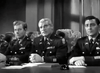 Three men in military uniforms sit at a table, serious and attentive, reminiscent of a WWII combat scene. The black and white photo captures the classic movie atmosphere of "Under Fire (1957)" DVD.