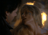 A man and woman stand close under dramatic, dim lighting, capturing the intense mood of a vampire detective film. The woman tilts her head back with closed eyes as flames burn in the blurred background. Product: Nick Knight (1989) DVD.