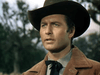 A man in a brown cowboy hat and jacket stands outdoors beneath a cloudy sky, channeling classic cowboy cinema as featured in Gun Belt (1953) DVD.