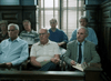 Seven people, mostly older men, sit closely in a wooden jury box—a scene reminiscent of rare courtroom movies on DVD like Judgement Day: The Ellie Nesler Story (1999), with notebooks and papers in hand and wood paneling behind them.