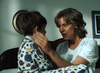 A woman in pajamas sits on a bed, comforting a young boy in printed pajamas—both appear emotional, reminiscent of tense scenes from Judgement Day: The Ellie Nesler Story (1999) DVD. The woman looks worried as she touches the boy’s face.
