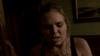 A worried blonde woman stands indoors, holding a phone and touching a wall—capturing the suspenseful mood of "Just What the Doctor Ordered (2021) DVD." Dim lighting and a framed picture add to this tense movie scene.