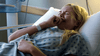 A distressed woman in a hospital gown and wristband lies in bed, covering her mouth as sunlight streams in—a dramatic moment from the film "Just What the Doctor Ordered (2021)" DVD.