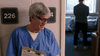 An older man in blue scrubs stands smiling near a door marked 226, holding a clipboard—much like a scene from Just What the Doctor Ordered (2021) DVD, a rare crime thriller. In the background, someone stands by a hospital bed.