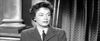 Black-and-white image of a woman with short, dark hair wearing a suit and tie, standing indoors in front of a column and curtains, looking slightly to the side with a neutral expression—a timeless scene evocative of classic WWII drama films like Bitter Victory (1957) on DVD.
