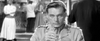 A man in a military uniform sits at a table, holding a glass and gazing ahead, while blurred figures and a chef appear in the background—a black-and-white scene reminiscent of classic films like “Bitter Victory (1957),” now available on DVD.