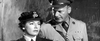 A woman in a military uniform stands beside a man in an officer’s uniform, both appearing serious in this striking black-and-white scene from Bitter Victory (1957) on DVD—a classic film that evokes the tension and drama of WWII.