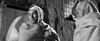 Two men, cloaked in heavy garments and blankets, stand solemnly outside a building at night in this striking black-and-white scene from “Bitter Victory (1957) DVD.” Both wear head coverings and one clutches his blanket tightly around his shoulders, capturing the haunting mood characteristic of this rare WWII drama—an elusive gem cherished by classic cinema collectors.
