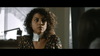 A startled woman with curly hair and a floral top sits indoors, her neck bandaged, in a tense scene from "I'll Take Your Dead (2018)"—a rare Canadian horror thriller now available on DVD.