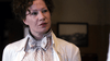 A woman with short curly hair wears a light coat over a checkered blouse with a bow, looking serious—an iconic image from the Madame Nobel (2014) DVD, ideal for any world cinema collection. A blurred frame is visible in the background.