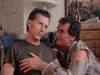 A man in a torn shirt kneels by another slumped in a chair, gently holding his chest with concern. A painting and dresser complete the scene from Promise (1986) DVD, echoing classic family drama and James Garner’s iconic roles.