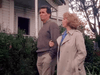 A man in a brown sweater and tan pants walks with a woman in a light trench coat outside a white house, reflecting the moving family drama portrayed in Promise (1986) DVD.