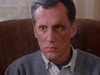 A man with short gray hair and a bruised face sits seriously on a brown chair—a scene reminiscent of family drama classics like the Promise (1986) DVD. Soft light filters through the window behind him.