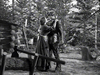 A man and woman embrace outside a rustic log cabin in a black-and-white outdoor scene from "The Iroquois Trail (1950) DVD," evoking the atmosphere of a classic frontier adventure.
