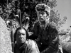 Two men in frontier attire crouch among rocks and trees, watching intently ahead in this black-and-white scene from The Iroquois Trail (1950) DVD—evoking the spirit of a classic frontier adventure.