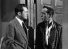 Two men in suits stand indoors, engaged in a serious conversation. The black-and-white scene captures the timeless style of "In A Lonely Place (1950)" DVD—an ideal choice for classic movie fans.