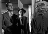 Two men in suits and hats stand at a doorway, speaking to a woman with short blonde hair. This dramatic black-and-white scene is from "In A Lonely Place (1950)" DVD, evoking classic film noir style with striking lighting and shadows.