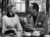 A woman in a light coat and a man in a suit sit at a table with teacups, framed by window blinds—a classic black-and-white moment from "In A Lonely Place (1950)" DVD.