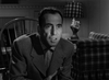 A man in a suit sits indoors, speaking intensely. Behind him are plaid chairs and a plaid-shaded lamp, echoing the vintage style of In A Lonely Place (1950) DVD—ideal for classic film enthusiasts.
