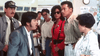 A group of people stand indoors, engaged in a tense conversation reminiscent of a classic Hong Kong action comedy. One man in a suit leans forward, speaking animatedly to a woman—his intensity echoing the charged scenes often featuring Cynthia Rothrock—while others watch closely, as if witnessing City Cops (1989) on DVD, one of those rare movies that keeps everyone on edge.