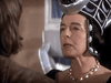 A person in an ornate black and silver headpiece and pearl necklace faces another person indoors, speaking seriously—evoking a scene reminiscent of an Arthurian legend film, such as the rare classic Sir Gawain and the Green Knight (2021) DVD.