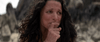 A woman with long dark hair looks concerned, holding her hand to her mouth against rocky terrain—a striking scene reminiscent of the film “Tuesday (2023)” now available on DVD.