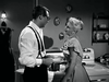A man in suspenders and a woman in a dress stand in a vintage kitchen, talking next to a stove. The black-and-white scene recalls the charm of classic movies from Hollywood’s golden era, like Monkey Business (1952) on DVD.