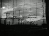 A train moves along tracks behind barbed wire under a cloudy sky at dusk, creating a somber and tense atmosphere reminiscent of scenes from “The Wooden Horse (1950)” on DVD.