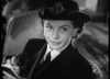 A woman in a black hat and coat sits indoors, looking upward as she writes in a notebook. Captured in striking black and white, the scene evokes classic moments from vintage cinema, reminiscent of the British naval war drama depicted in “Glory at Sea (1952)”—now available on DVD.