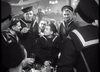 A group of sailors in uniform gather around a table in a lively setting—some holding drinks and smiling, with dim lights in the background—evoking the camaraderie and spirit depicted in classic WWII naval films like “Glory at Sea (1952)”, now available on DVD.