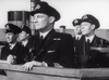 Five uniformed naval officers stand on a ship’s deck, looking ahead, capturing the suspenseful atmosphere of a British naval war drama as seen in “Glory at Sea (1952)” on DVD. The officer in front holds binoculars, scanning the horizon for danger—reminiscent of classic WWII minesweeper movie scenes. Parts of the ship and sky are visible in the black-and-white image.
