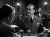 A man in uniform with an eye patch speaks in a crowded courtroom while another sits at a desk—a gripping scene from Operation Secret (1952) DVD, the classic WWII espionage thriller.