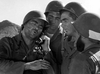 Four soldiers in helmets, their faces set with determination, stand together outdoors in this gripping scene from the rare classic Hell Squad (1958) DVD. One soldier speaks into a field telephone as the others listen intently, perfectly capturing the tense atmosphere typical of 1950s war films. In the background, a mountain rises dramatically, heightening the suspense and evoking the intensity of WWII action movies.