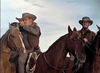 Two cowboys on horseback, one aiming a rifle while the other looks on. Both wear hats and western attire, with ropes hanging from their saddles, set against a backdrop of blue sky and open landscape—capturing the adventurous spirit found in rare classic films like *Southwest Passage (1954)*, now available on DVD.
