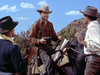 Three men in Western attire talk outdoors. One man on horseback holds a pistol, facing two others, with blue sky and rocky hills in the background—a memorable scene for fans of rare classic films and hard-to-find movies like the Southwest Passage (1954) DVD.