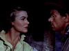 A woman and a man face each other closely, both with serious expressions. The woman wears a yellow shirt, while the man sports a cowboy hat and bandana, evoking a dramatic moment reminiscent of scenes found in classic films like “Southwest Passage (1954)”, now available on DVD.