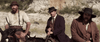 Three men dressed in old-fashioned Western attire sit on horses outdoors, framed by a rocky hill and sparse vegetation, capturing the rugged spirit of classic cinema as seen in *Kill or Be Killed (2015)* on DVD. A dog stands in the background, enhancing the timeless atmosphere.