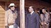 Three men stand outside a wooden building; one wears a cowboy hat and smokes, another is dressed in a suit, and the third stands in a vest, watching the scene unfold. Capturing the gritty ambiance of rare classic movies, this image looks as if it’s straight from a Western—fitting for “Kill Johnny Ringo (1966)” available on DVD.