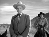 An older man in a suit and cowboy hat sits on a horse in the foreground, while another man in western attire rides behind him against a desert landscape—a scene reminiscent of the classic film Along the Great Divide (1951) DVD starring Kirk Douglas.