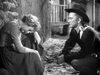 A woman sits on a stone path, head bowed and face in her hand, while a man in a cowboy hat crouches nearby, watching her with concern—evoking the emotional depth often seen in “Along the Great Divide (1951)” on DVD.