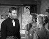 Three people in old-fashioned western attire stand in a room with patterned wallpaper, facing each other in conversation. Two men are talking while a woman looks on from the side—a striking scene from “Badman’s Country (1958) DVD,” making it perfect for fans of classic western DVD collections or collectors seeking rare movies on DVD.