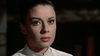 A woman with dark hair pulled back gazes forward with a serious expression, dressed in a light-colored, striped collared shirt against a dark background—her poised demeanor calling to mind classic film characters from 1960s westerns such as those featured in *Five for Revenge (1966) DVD*.