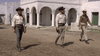 Three men in cowboy hats and western attire walk side by side through a dusty courtyard with white adobe-style buildings and arched columns in the background—a scene straight out of 1960s western cinema, making “Five for Revenge (1966) DVD” a must-have for classic movie enthusiasts.