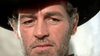 A close-up of a rugged-faced man with a gray beard and mustache, wearing a black hat, gazes seriously and contemplatively in bright sunlight—a scene evocative of classic 1960s westerns like “Five for Revenge (1966)” on DVD.